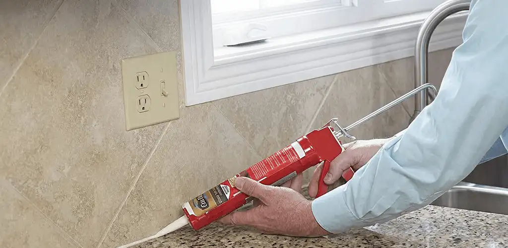 Handyman applying caulk along a kitchen backsplash and countertop seam in Provo, UT